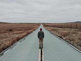 Man standing in middle of road by fields, rear view 