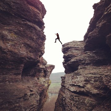 Person in mid air, leaping in between cliffs 