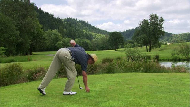 Golfer teeing up ball, hitting it down fairway, and walking out of frame at left