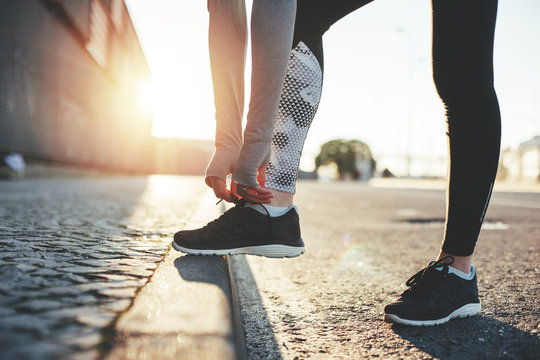 Female urban athlete ties up the shoelaces on the city street. Sport tight clothes
