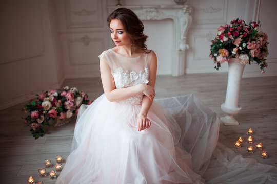 Girl with makeup in a pink wedding dress is sitting in a beautiful room surrounded by flowers and candles