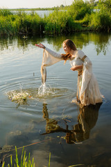 Pretty young woman in traditional dress puts wreath in water of lake. Russian traditional Ivan Kupala holiday celebration