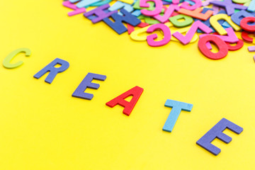 Colorful wooden alphabet and word "CREATE". Top view on yellow table