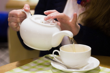 A girl pours tea from a teapot into a mug