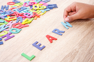 Colorful wooden alphabet and word "LEARN", Hand sort on N. Top view on grey wooden table