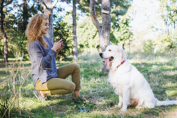 Young female taking photo of labrador retriever dog in park