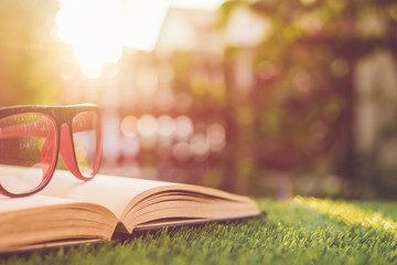 Glasses and book on green grass with blur and bokeh in sunrise time background