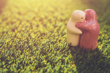 White and pink ceramic doll on green grass with blur bokeh and sunlight