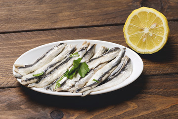 Plate of anchovies with olive oil, vinegar and lemon. Half lemon.