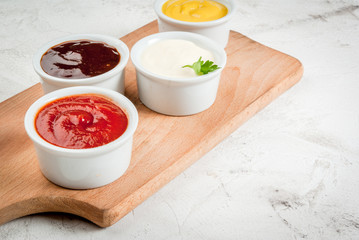 Classic set of sauces in white saucers: American yellow mustard, ketchup, barbecue sauce,...