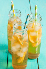 Iced summer drink - tea with lemon on a blue wooden table, in bottles with striped straws copy space