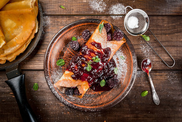 Delicious homemade breakfast: french crepes with forest fruit, topped with jam and filled with forest fruit, sugar and mint, wooden table