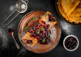 Delicious homemade breakfast: french crepes with forest fruit, topped with jam and filled with forest fruit, sugar and mint, black concrete table