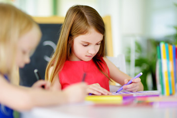 Two cute little sisters drawing with colorful pencils at a daycare. Creative kids painting together.