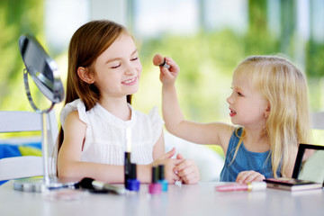 Two cute funny sisters applying make-up on sunny summer day at home