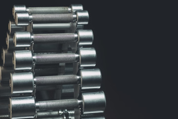 Metal dumbbells on an iron stand in a sports hall, close-up on a black background. Sports concept, fat burning and healthy lifestyle.
