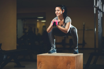 Slim girl bodybuilder jumping on a wooden box in front of the mirror while training in the gym. Sports concept, fat burning and a healthy lifestyle.