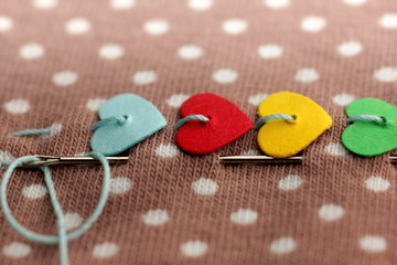 macro of colorful hearts stitched on dotted fabric with needle and thread - backgrund and...