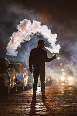 The man smoke electronic cigarette in the street. Evening night time
