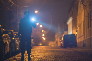 The man with a flashlight stand on the street. Evening night time - obrazy, fototapety, plakaty
