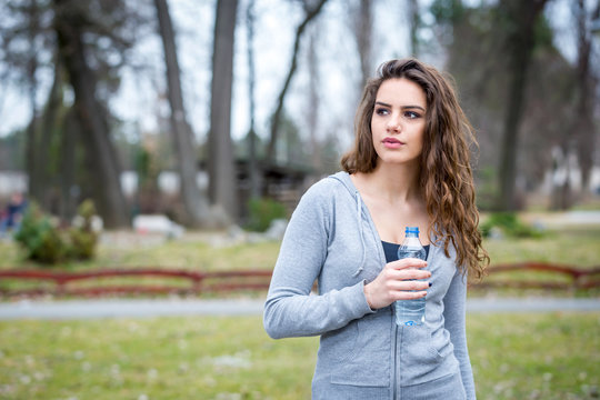 young woman holding bottle of water in a park