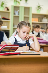 little beautiful schoolgirl in school uniform with brunette hair sitting on desk