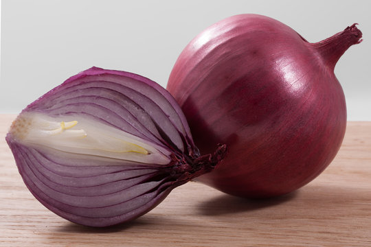 A raw purple onion with sliced pieces on a wooden background.