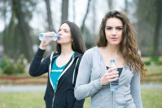 two young woman drinking water in a park