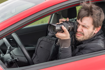 Stalker or paparazzi is taking photo with camera from car.