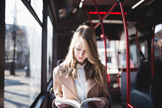 Beautiful young woman sitting in city bus and reading a book. 