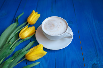 Coffee mug with yellow tulip flowers and notes good morning on blue rustic table from above, breakfast on Mothers day or Womens day .Spring  flowers bouquet