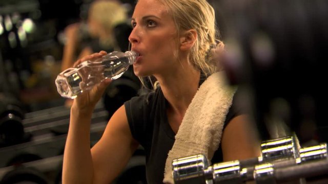 Perspiring young woman drinking from water bottle after weight room workout