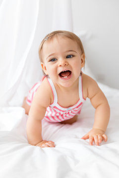 happy baby girl crawling on a white bed with her mouth open