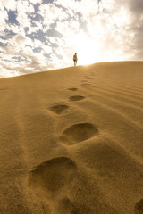 girl walks on sand dunes, uphill