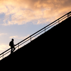 Silhouette of Man climbing the way or steps over sunset sky background.