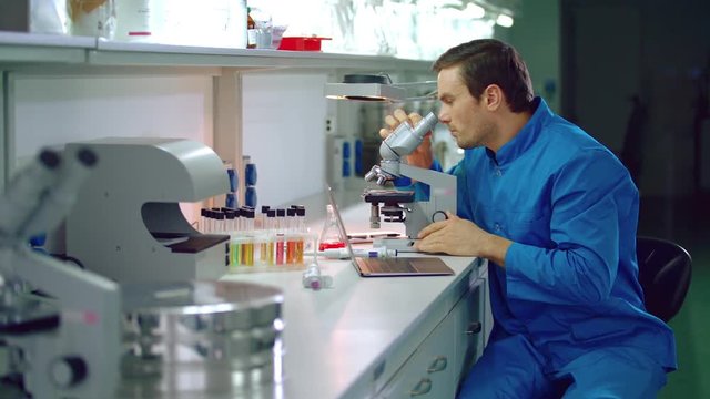 Lab doctor looking microscope. Laboratory doctor using laptop in medical lab. Medical researcher looking through microscope. Clinical laboratory research. Lab worker using medical microscope