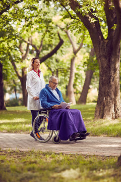 Nurse pushing elderly man in wheelchair while reading book .