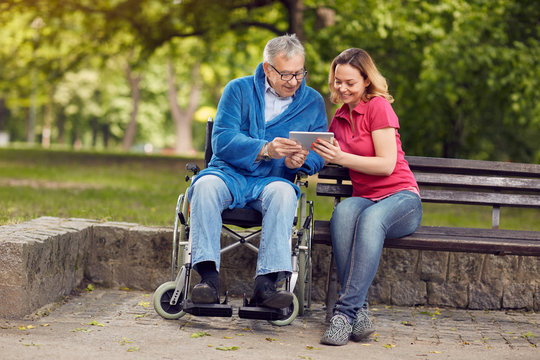 Happy wheelchair man with daughter using tablet.
