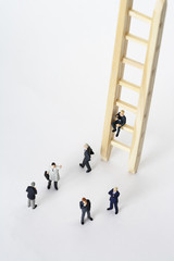 Businessmen figurines standing next to a ladder, one figurine sitting on a rung