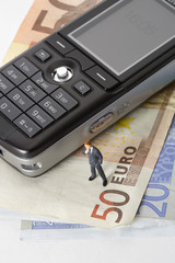 Businessman figurine next to mobile phone on a stack of Euro banknotes