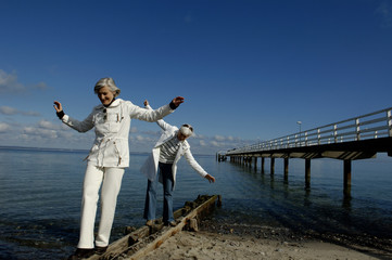 Two mature women balancing over a beam at Baltic Sea beach