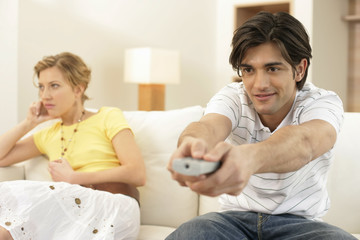 Young man watching TV, bored young woman sitting in background