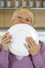 Blond woman holding a plate to her mouth, close-up