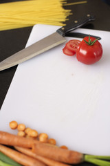 Tomato and carrots on a carving board next to a kitchen knife, high angle view