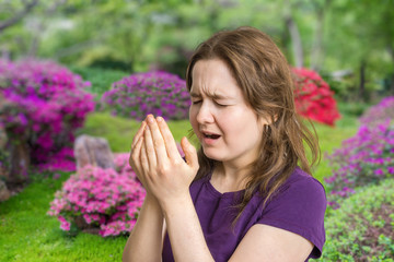 Pollen allergy concept. Young woman is going to sneeze. Flowers in background.