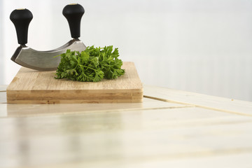 A kitchen board with parsley and mezzaluna chopper