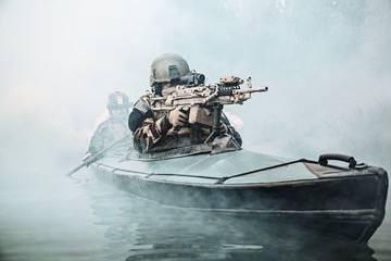 Special forces marine operators in camouflage uniforms paddling army kayak through river fog....