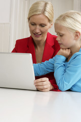 Blond girl is sitting next to her mother behind a laptop, close-up