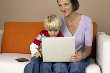 Mother and son (4-5 Years) sitting on a sofa und using a laptop