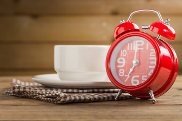 Red alarm clock with coffee cup on wood table.